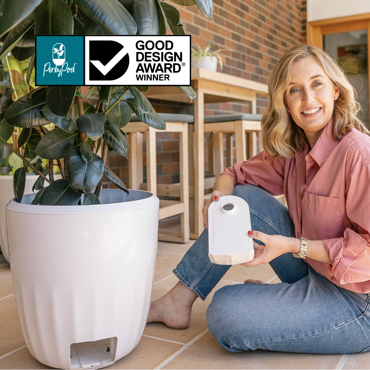 Woman holding the PerkyPod water catchment drawer next to a plant with Good Design Award logo in the corner. It is better than a self watering plant pot as water can be removed.