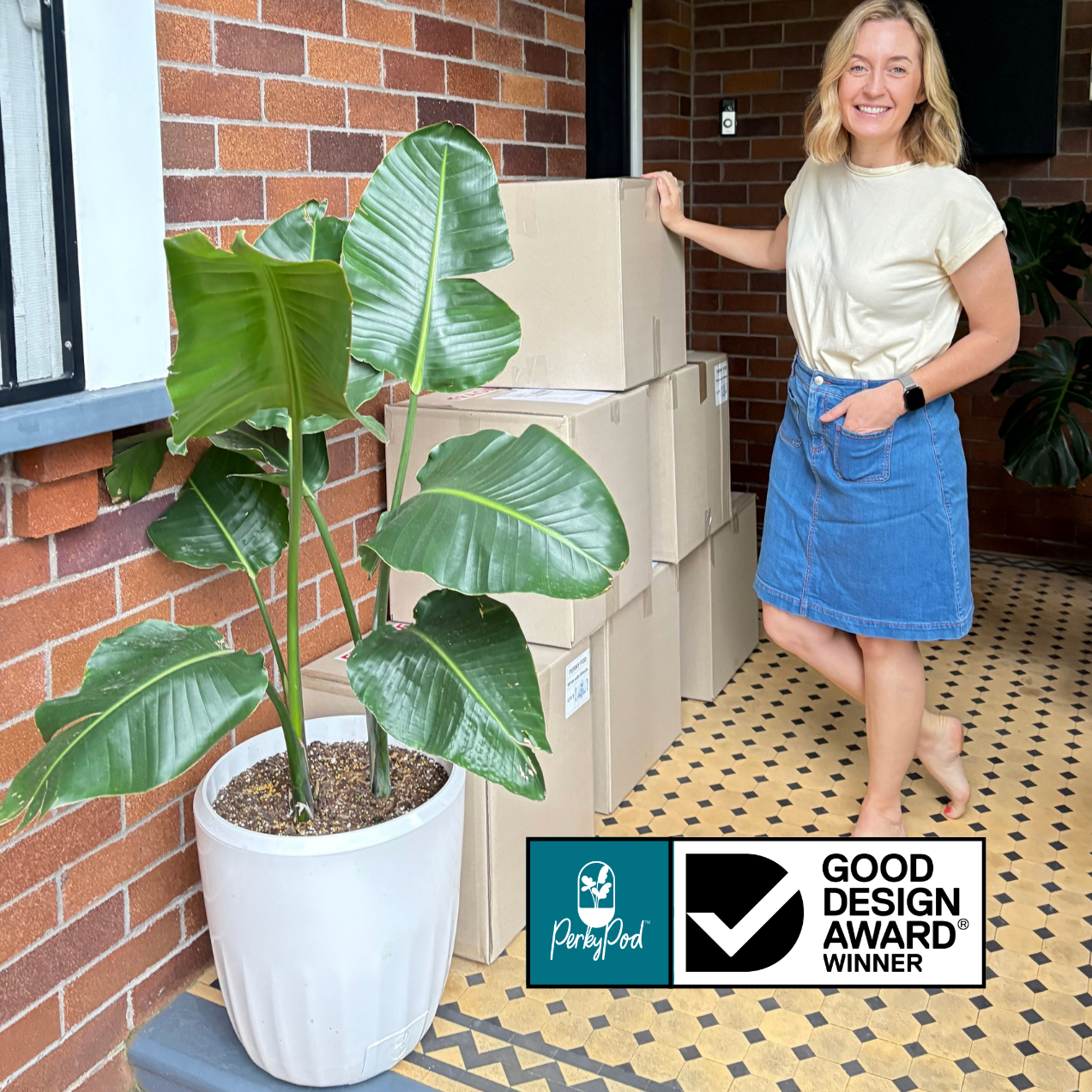 Woman standing next to stacked boxes on her front porch with a potted plant in PerkyPod. Ready for pick up by a courier. Good Design Award logo visible