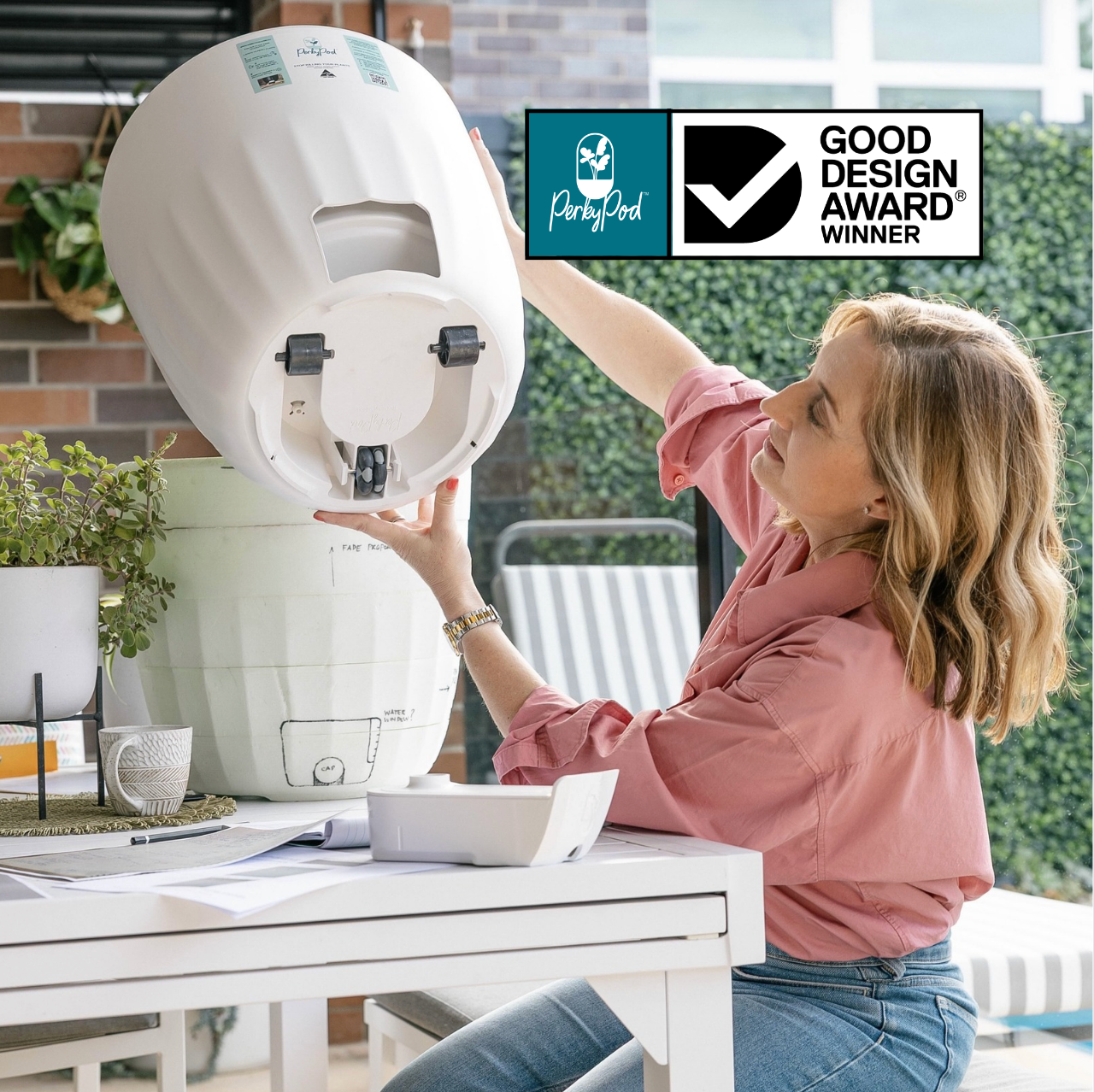 Woman interacting with a white PerkyPod plant pot on a table showing concealed wheels underneath